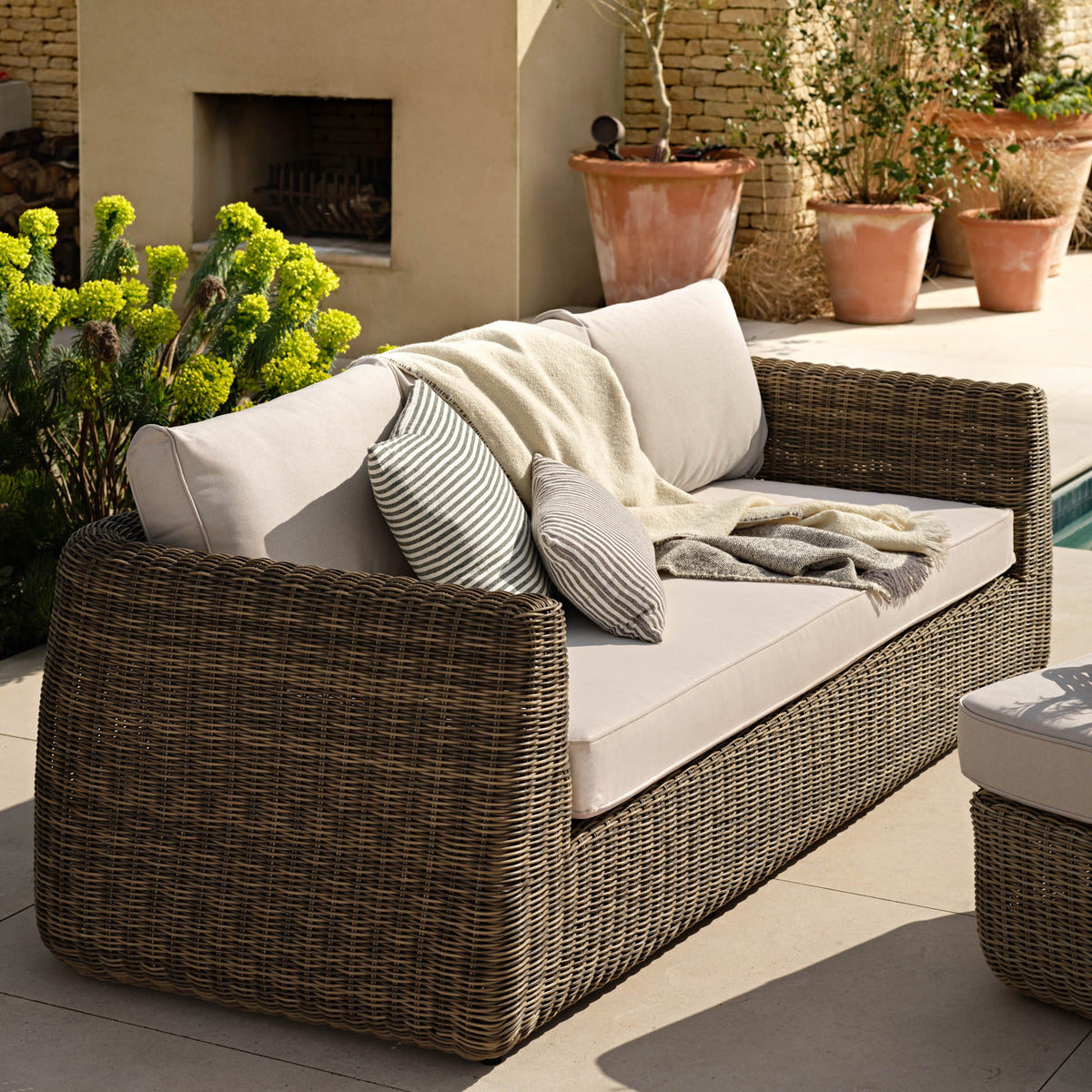 Outdoor patio scene with wicker sofa, cushions, and potted plants.