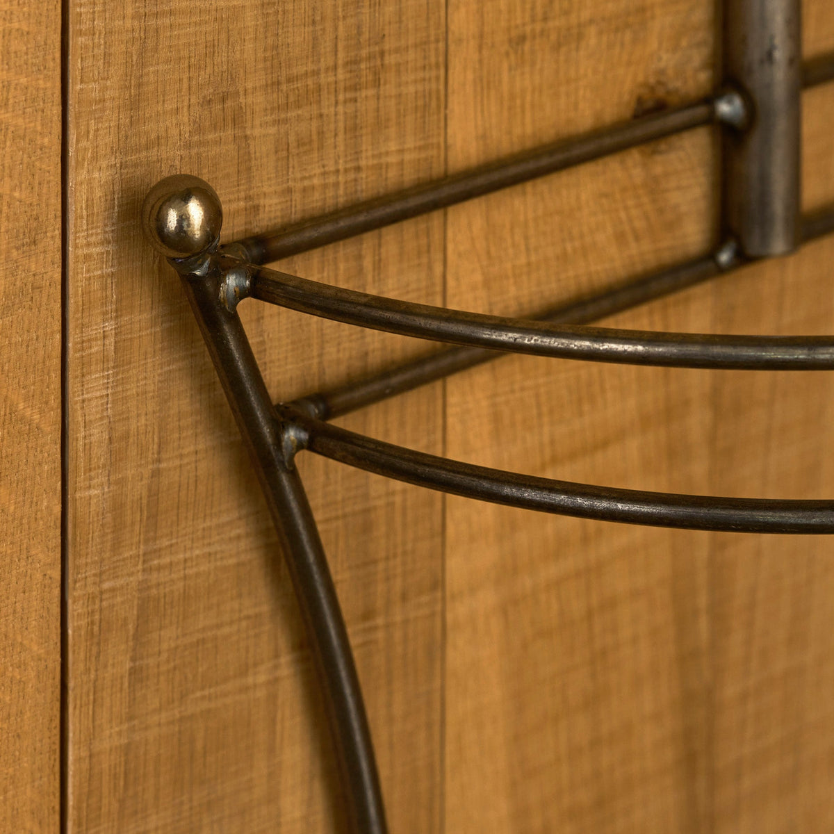 Close-up of a dark metal wire rack or shelf mounted against a warm wood-paneled wall.