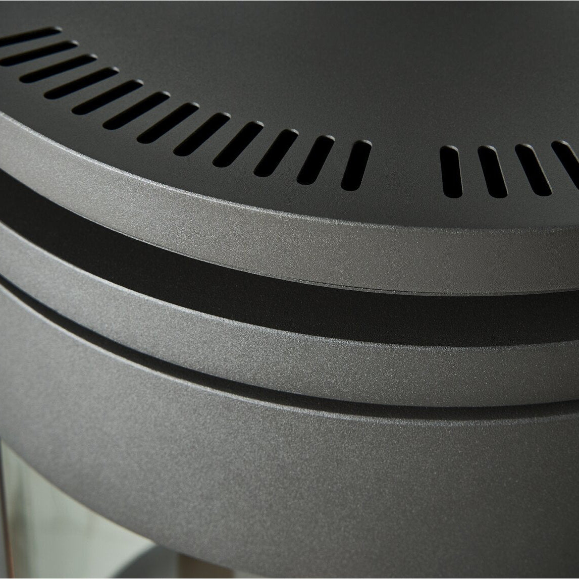 Close-up detail of a dark gray cylindrical product, showing a perforated circular top vent and horizontal slotted bands on a matte finish.