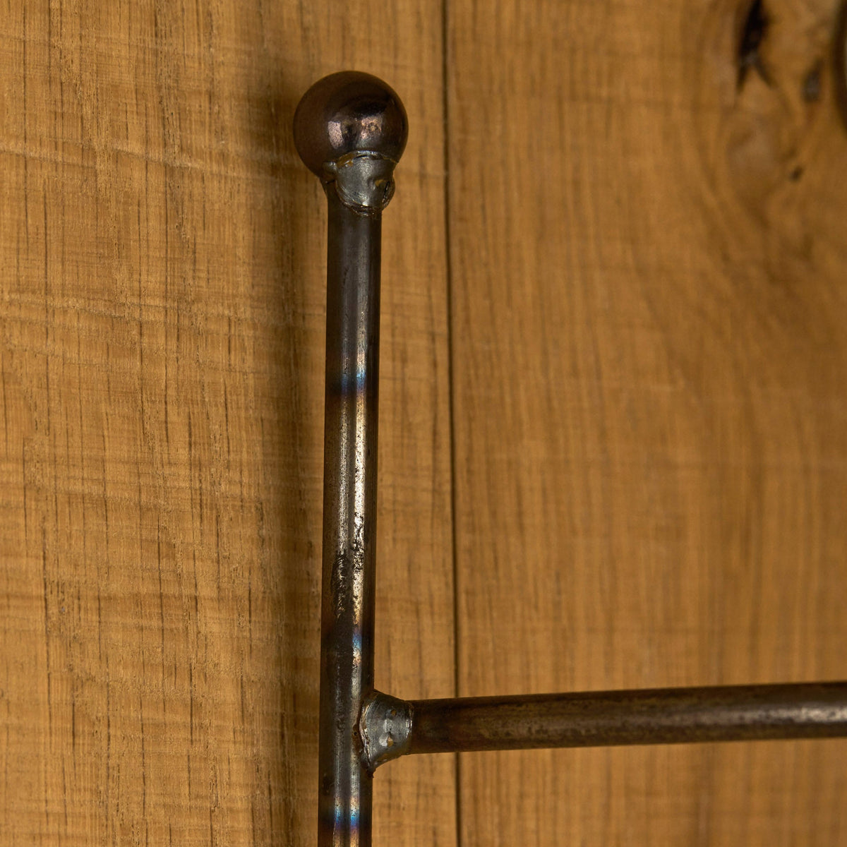 A close-up of a dark metal bed frame rail with a spherical finial and horizontal support bar, set against a warm wood plank background.
