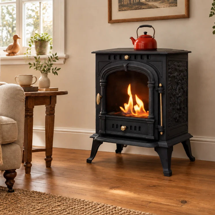A black traditional scandinavian cast iron bioethanol stove with a glowing fire inside, set in a cozy living room next to an armchair and a wooden side table.