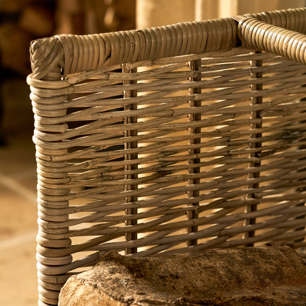 Close-up of a woven rattan chair back with a rustic wooden log resting on the seat, photographed in warm natural light.