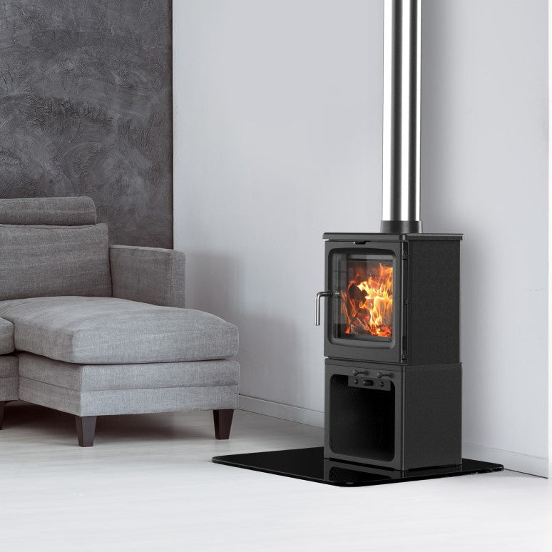 A modern black wood-burning stove with a visible fire, positioned next to a gray sectional sofa in a minimalist living room setting.