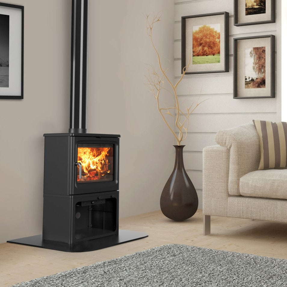 A black wood-burning stove with a visible fire, set in a modern living room next to a beige sofa and a gray rug.