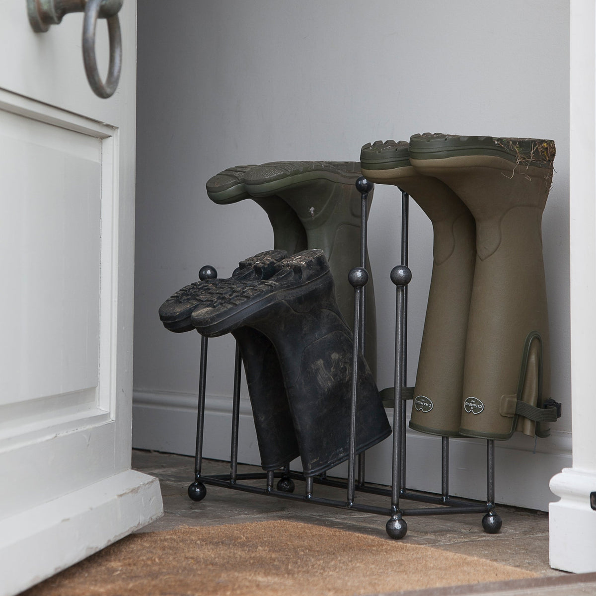 Pair of green rubber boots on a metal boot rack by a door.