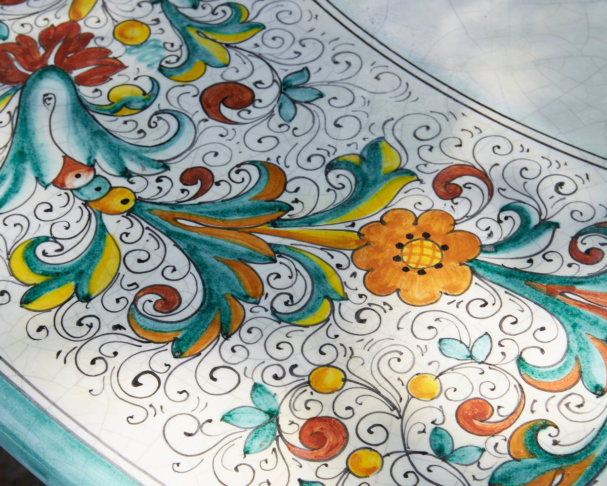 Close-up of a round table featuring a white base decorated with a colorful hand-painted floral and scroll pattern in teal, orange, yellow, and red.